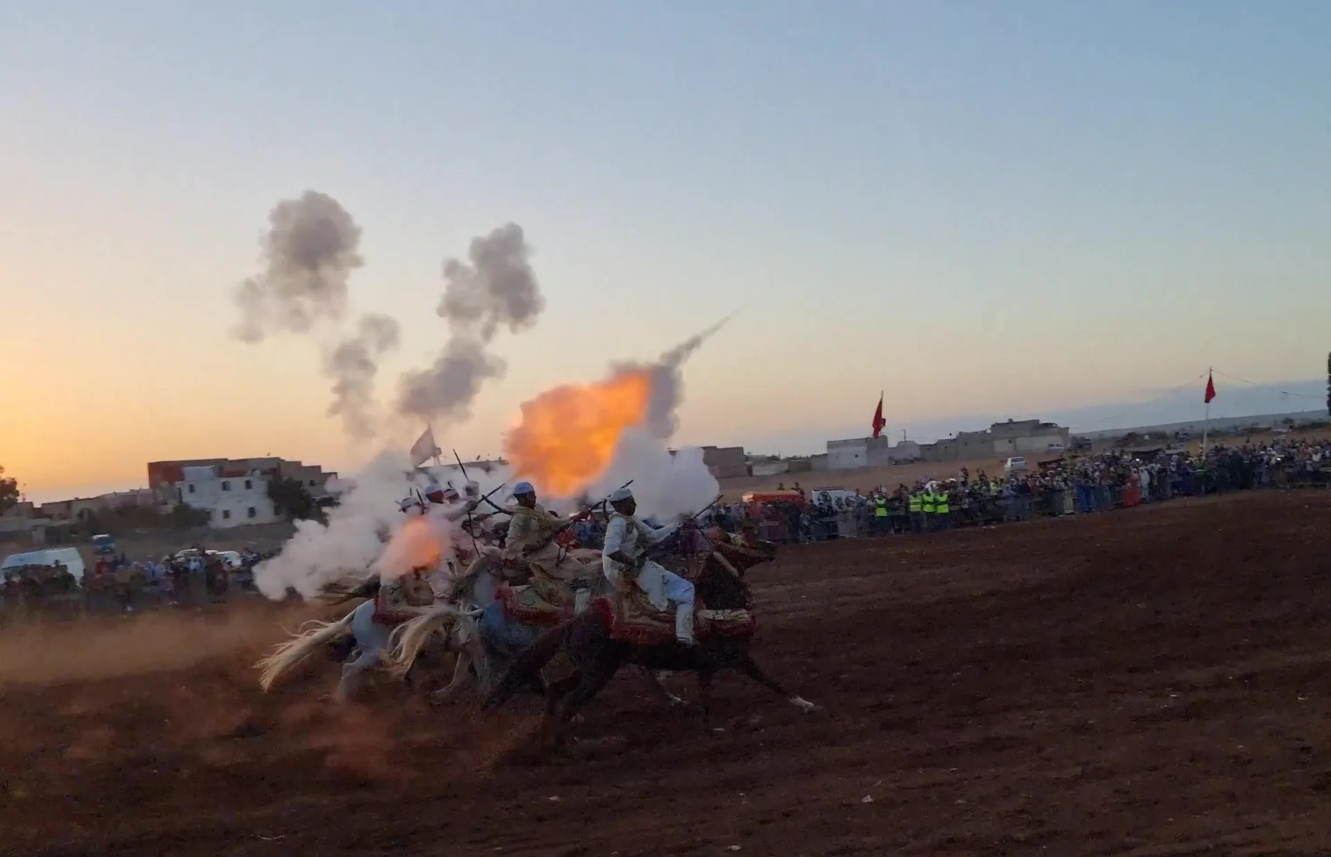 Moroccan horsemen firing rifles in unison during a Fantasia (tbourida) charge at sunset